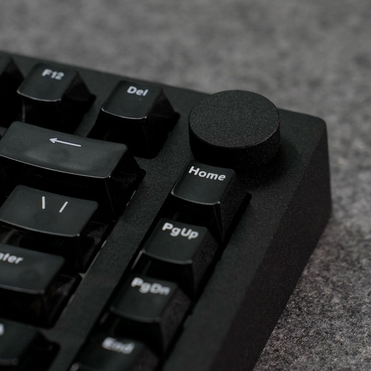Close-up of a black MonsGeek M1 V5 HE Magnetic Keyboard with focus on keys like 'Home' and 'PgUp' on a textured surface.